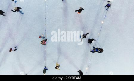 La gente pattina sulla pista di pattinaggio all'aperto nella notte d'inverno vista dall'alto. Vista aerea del drone. Luci luminose per ghirlande. Proietta ombre lunghe. Capodanno festa di Natale ricreazione Foto Stock