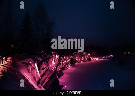 Bella vista panoramica del parco notturno con luci colorate Viva Magenta sulla foresta invernale e rocce, Ruskeala, Carelia, Russia. Design creativo alla moda a colori 2023. Foto di alta qualità Foto Stock