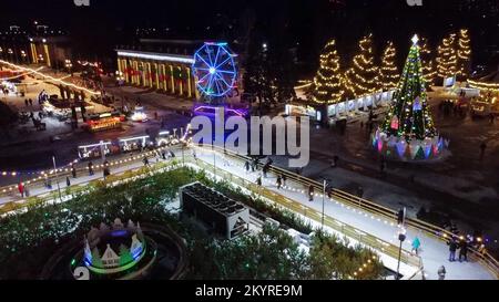 Molta gente pattina sulla pista di pattinaggio di ghiaccio bella in aria aperta decorata luci di Natale di Capodanno, decorazioni, ghirlande luminose nella notte di inverno. Festa di Natale di Capodanno. Antenna Foto Stock