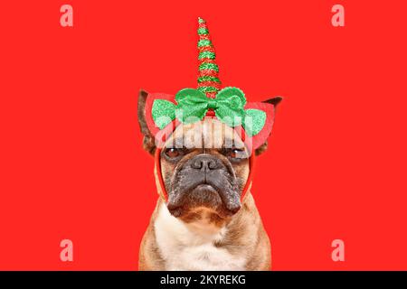 Cane Bulldog francese con fascia di unicorno di Natale di fronte a sfondo rosso Foto Stock