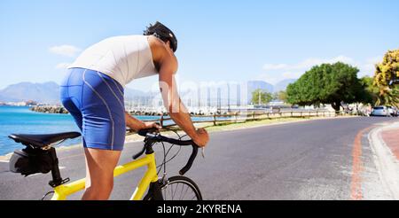 Godendo il paesaggio mentre si esercita. Vista ritagliata di un ciclista che pedeggia lungo una strada oceanica. Foto Stock