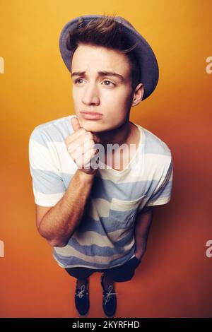 Mulling le cose sopra. Studio shot di un giovane uomo in un cappello con un espresone facciale perplesso. Foto Stock