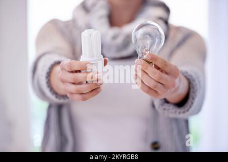 Scegliete l'ambiente. Immagine ritagliata di una donna che tiene due lampadine diverse. Foto Stock