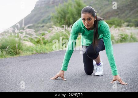 Pronto a rendere questa strada sua... Una giovane donna accovacciata sulla strada che sta per andare per una corsa. Foto Stock