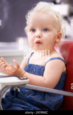 Posso nutrirmi. Un bambino piccolo felice che mangia gli alimenti solidi mentre si siede su una sedia alta. Foto Stock