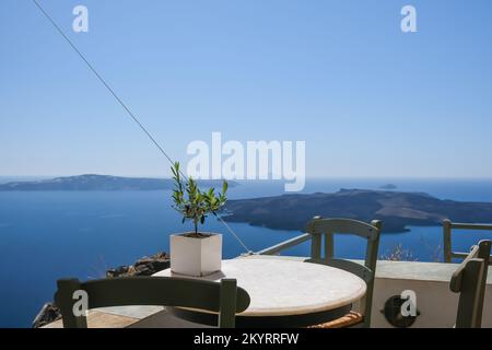 Vista su un tavolo con sedie decorato con un piccolo ulivo in vaso e una splendida vista su Santorini Foto Stock