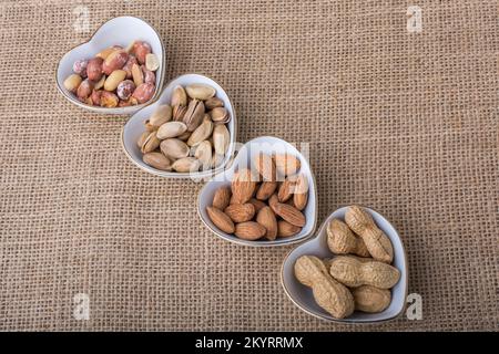 Arachidi, mandorle, pistacchio in piatti a forma di cuore su tela Foto Stock