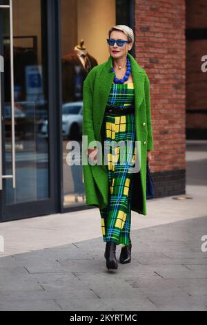 Ritratto integrale di donna adulta alla moda con un lungo cappotto verde e un abito elegante. Tendenza alla moda per l'autunno o la primavera. Elegante vestito da donna con blu Foto Stock