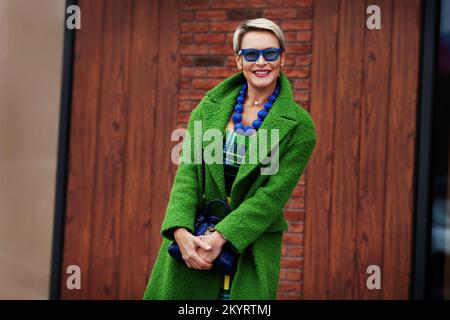 Ritratto di donna sorridente elegante vestito verde con accessori blu. Abito casual colorato e alla moda. Modello felice di 45-50 anni con fash corto Foto Stock