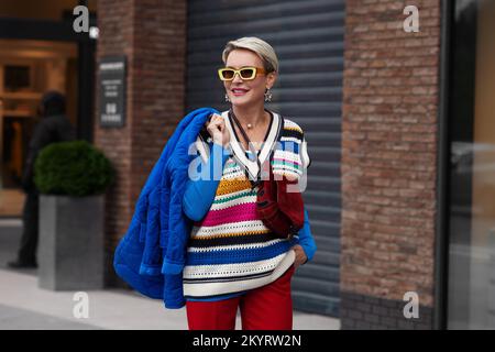 Sorridente Happy Model indossa giacca e maglione blu, doratura a righe, pantaloni rossi e occhiali da sole gialli. Moda Street stile autunno o primavera. Donna p Foto Stock