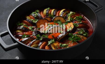 Ratatouille a strati in una teglia da forno, fette di zucchine, peperone rosso, peperoncino, zucca gialla, melanzane, olio d'oliva, prezzemolo e aglio Foto Stock