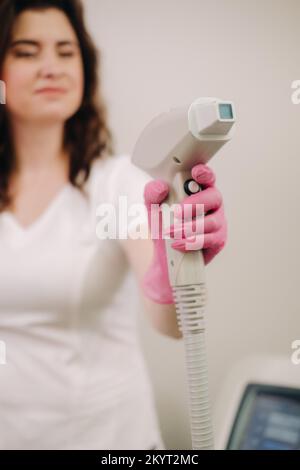 Ritratto del maestro della rimozione dei peli del laser. Una donna in un cappotto bianco tiene un dispositivo di rimozione dei capelli del laser nelle sue mani Foto Stock