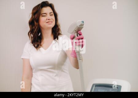 Ritratto del maestro della rimozione dei peli del laser. Una donna in un cappotto bianco tiene un dispositivo di rimozione dei capelli del laser nelle sue mani Foto Stock