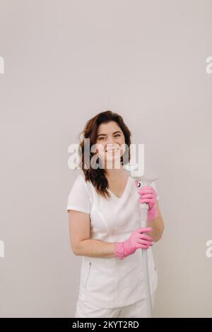 Ritratto del maestro della rimozione dei peli del laser. Una donna in un cappotto bianco tiene un dispositivo di rimozione dei capelli del laser nelle sue mani Foto Stock