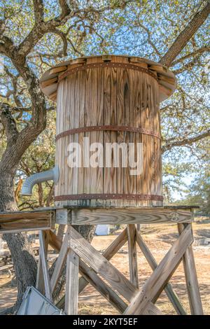 Piccolo vecchio serbatoio di legno con tubo contro gli alberi e cielo blu in una giornata di sole. Vista ravvicinata di un collettore d'acqua cilindrico vintage contro una scen Foto Stock
