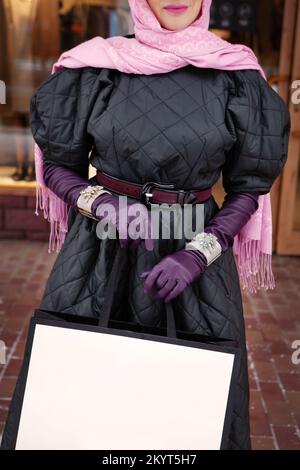 Donna che tiene la borsa della spesa, indossando eleganti guanti e braccialetti in pelle, elegante sciarpa per la testa e cappotto trapuntato. Abbigliamento femminile alla moda e accessori Foto Stock