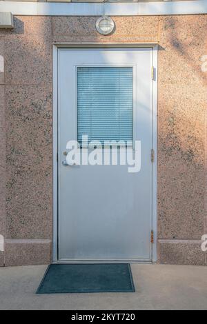 Porta bianca con vetro contro le pareti di cemento rossiccio di un vecchio edificio. Vista a Austin, Texas, con primo piano su una porta chiusa con ciechi bianchi Foto Stock