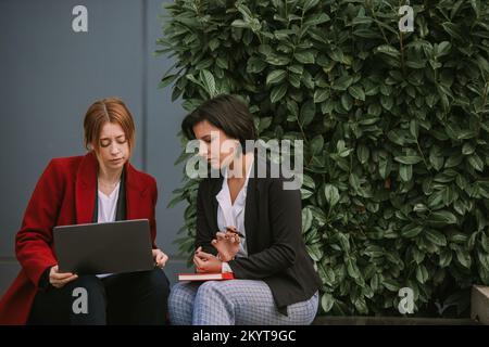 Primo piano di due straordinarie donne in viaggio d'affari che guardano il notebook mentre si siedono sulla panca Foto Stock