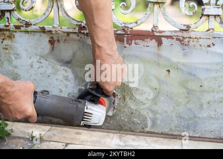 L'uomo di mano scrape la vecchia vernice dal recinto arrugginito Foto Stock