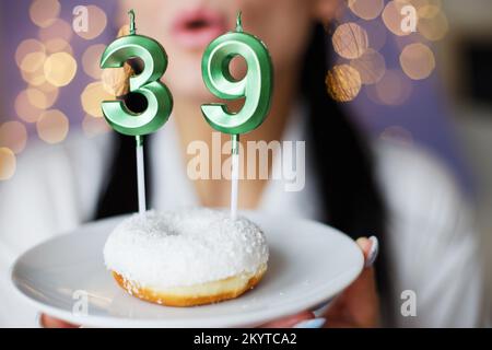 donna che tiene una torta con il numero 39 candele su sfondo bokeh sfocato festivo. Foto Stock