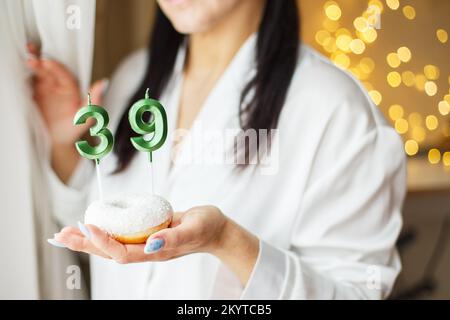 donna che tiene una torta con il numero 39 candele su sfondo bokeh sfocato festivo. Foto Stock