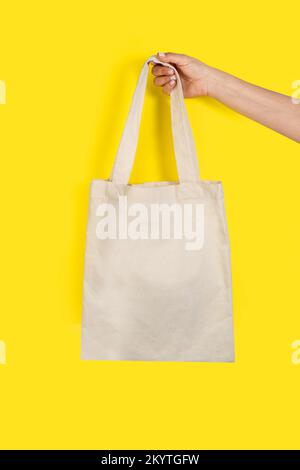Mano donna che tiene una borsa tote bianca su sfondo giallo con spazio per le copie Foto Stock