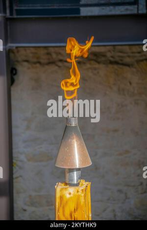 Fiammella su un kit torcia su un legno a San Antonio, Texas. Primo piano selettivo di una fiamma da fuoco su una torcia contro lo sfondo sfocato della parete. Foto Stock