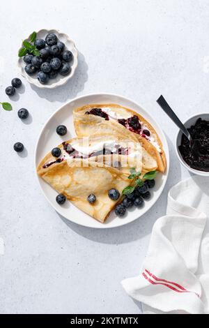 Crepes con confettura di mirtilli, ricotta e frutti di bosco freschi. Frittelle dolci per colazione. Vista dall'alto Foto Stock