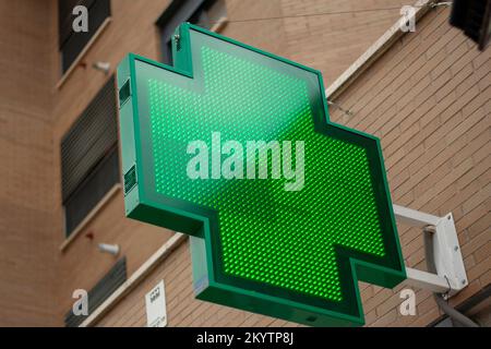 Croce verde luminosa che indica che una farmacia rimane aperta nella città di Madrid Foto Stock