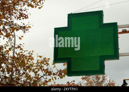 Croce verde luminosa che indica che una farmacia rimane aperta nella città di Madrid Foto Stock