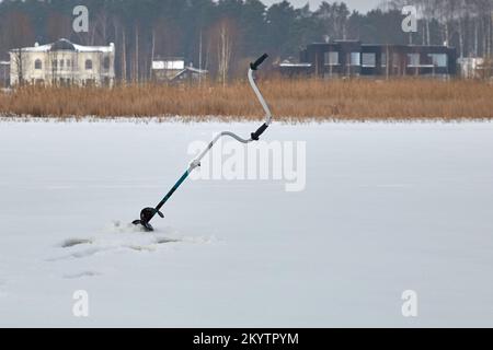 21 gennaio 2021, Baltezers, Lettonia: Perforatore di ghiaccio del pescatore su un lago ghiacciato da un lato posteriore Foto Stock