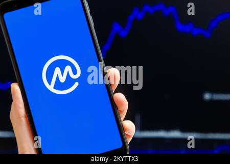 Ucraina, Odessa - Ottobre, 9 2021: Tenere a mano mobile con l'app CoinMarketCap in esecuzione sullo schermo dello smartphone, trading candelabro grafico in background. L'autorità di crittografia dei dati più affidabile al mondo Foto Stock