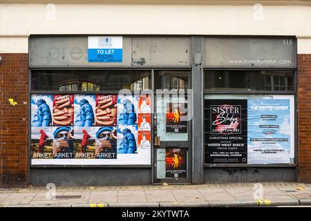 Un uomo che passa davanti a un negozio chiuso con le sue finestre coperte poster di fattura, Clerkenwell Road, Londra, Regno Unito. 20 Nov 2022 Foto Stock