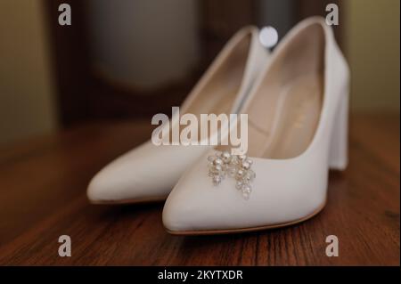 Orecchini con perle su scarpe bianche da donna in pelle. Accessori della sposa, mattina della sposa. Foto Stock