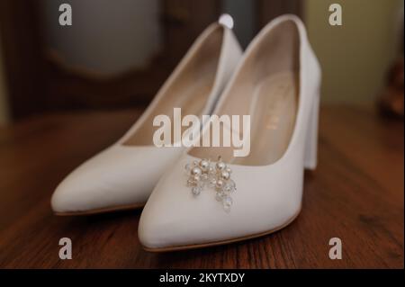 Orecchini con perle su scarpe bianche da donna in pelle. Accessori della sposa, mattina della sposa. Foto Stock