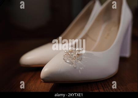 Orecchini con perle su scarpe bianche da donna in pelle. Accessori della sposa, mattina della sposa. Foto Stock