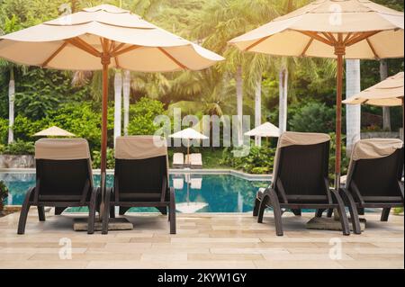 Sedie a sdraio e ombrellone accanto alla piscina nel resort dell'hotel nelle giornate di sole Foto Stock