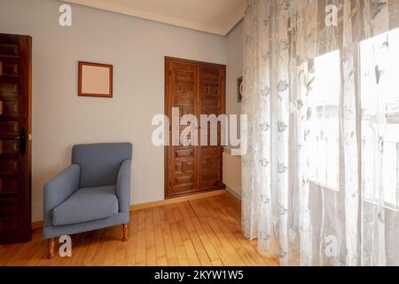 Angolo di una camera da letto con pavimento in legno naturale, armadio a muro con porte a pannelli e poltrona singola in tessuto blu Foto Stock