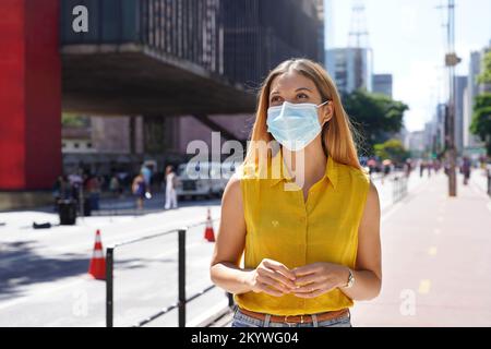 Bella giovane donna che cammina su Paulista Avenue indossando una maschera chirurgica a San Paolo, Brasile Foto Stock