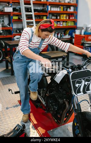 Donna meccanica che inizia motocicletta personalizzata in fabbrica Foto Stock