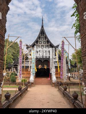 Vista verticale dell'antico vihara in legno in stile Lanna attraverso le mura del cancello d'ingresso dello storico tempio buddista Wat Lok moli, Chiang mai, Thailandia Foto Stock