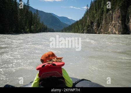 Un bambino in giubbotto di salvataggio siede sulla prua di una zattera in un ampio fiume Foto Stock