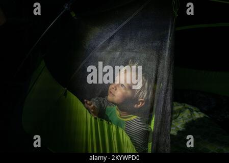 Un ragazzo guarda da una tenda a rete di notte Foto Stock