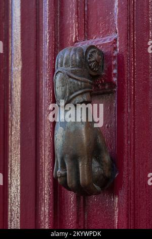 Vista in primo piano di un elegante knocker porta in ottone vintage a forma di mano che tiene la palla isolato sulla porta di legno rosso scuro, Montpellier, Francia Foto Stock