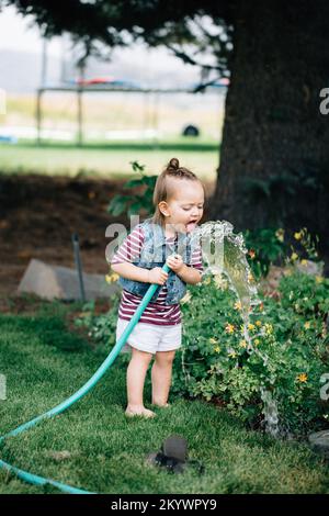 Bambina che beve acqua da una manichetta fuori dal giardino Foto Stock