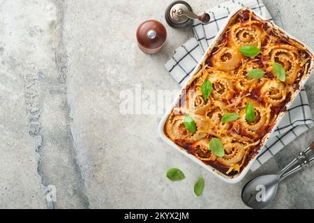 Lasagne. Lasagne fatte in casa - rotolo di pasta con salsa di pomodoro, crema di formaggio e basilico su padella bianca su fondo di ardesia leggera, pietra o cemento. IO Foto Stock