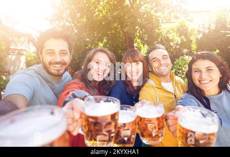 Gruppo di amici che brindano bicchieri da birra all'aperto nella fattoria - Gruppo di studenti che si divertono alla festa di compleanno nel ristorante giardino Foto Stock