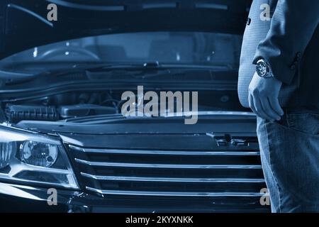 Uomo che guarda il motore di una macchina con cofano aperto Foto Stock