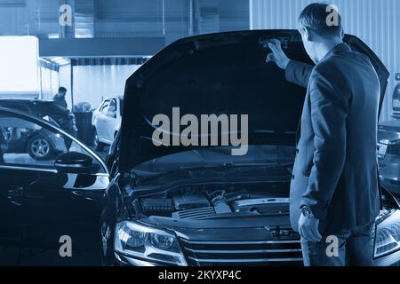 Uomo che guarda il motore di una macchina con cofano aperto Foto Stock