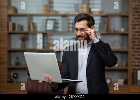 Maturo avvocato uomo d'affari lavora in ufficio cameriere utilizza computer portatile, capo senior in occhiali e business suit sorridente uomo in ufficio. Foto Stock